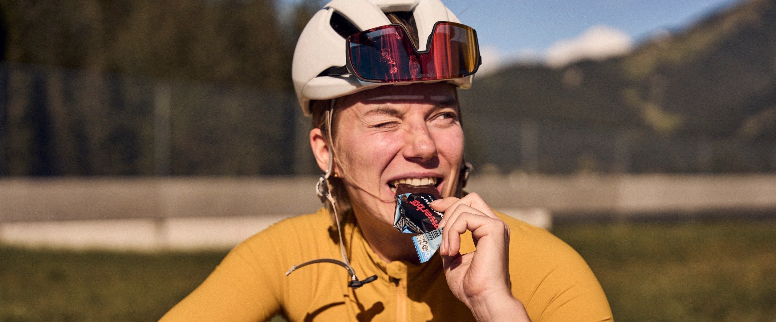 Cyclist in yellow jersey eating a Powerbar energy bar.